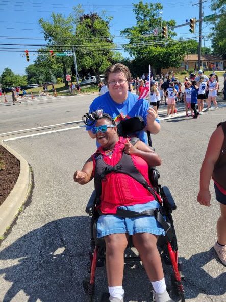 man pushing woman in a wheelchair both smiling and wearing festive fourth of july gear